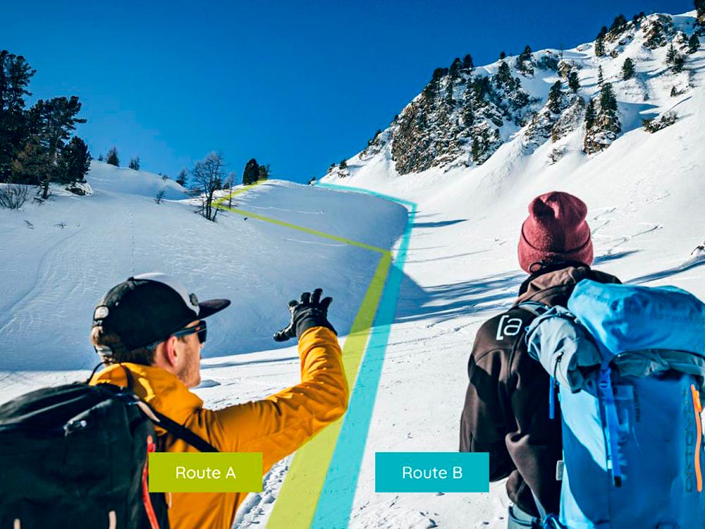 Zwei Personen stehen vor einem verschneiten Hang und diskutieren zwei markierte Aufstiegsrouten: Route A (grün, links, flacher) und Route B (blau, rechts, steiler). Schneebedeckte Bäume und ein klarer Himmel bilden den Hintergrund.